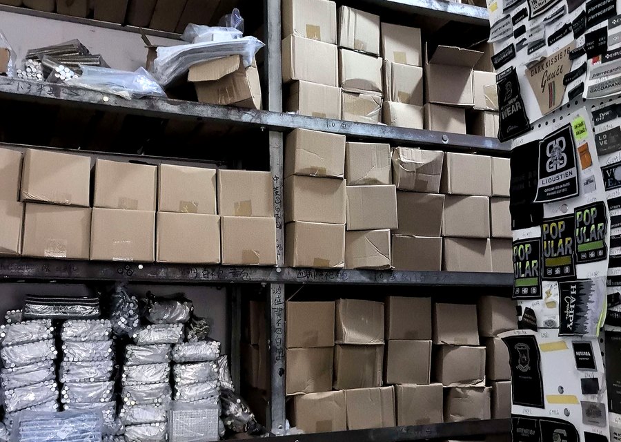 钱浩辅料现货仓库：纸箱码放的吊牌与织唛成品货架，墙面贴标分类